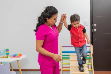 Nurse helping a child walk through a wooden game, which is in her medical office.