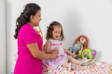 Little girl blowing while being checked by a pediatrician doctor in her medical office.