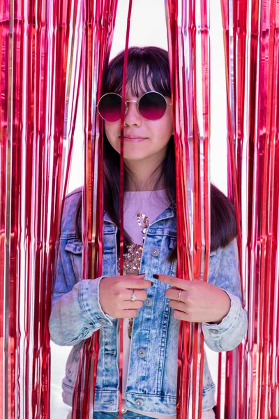 Portrait of teenage girl with glasses behind a metallic pink party curtain.