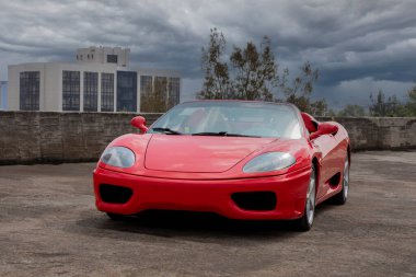 Red sports car on a city rooftop with buildings and cloudy sky in the background.