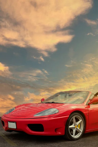 Vertical shot of the front of a red sports car with the sunset in the background and copy space.