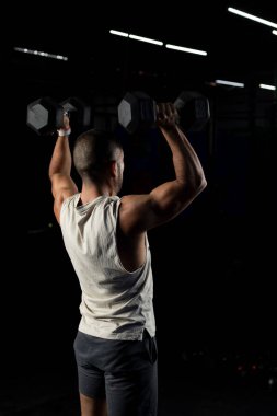 İki dambılı iten kaslı bir adamın dikey görüntüsü.