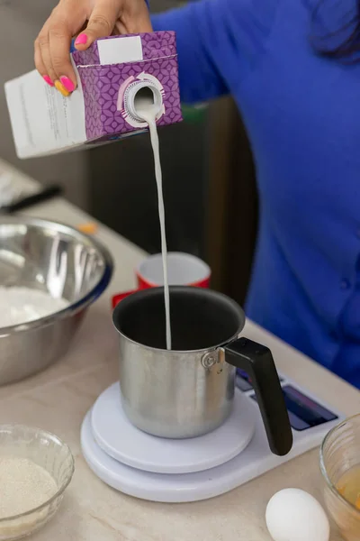 womans hand pouring milk into a container to weigh on a scale and make bread