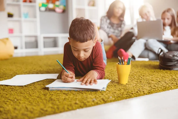 Iskolásfiú kezében egy ceruza és rajz papíron a padlón — Stock Fotó