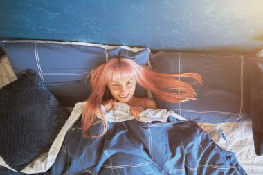 Neşeli bayan yumuşak yorganın altında yumuşak yastıklarla rahat bir yatakta yatıyor.