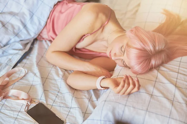 Zmęczona kobieta z różowymi włosami śpi z telefonem komórkowym w wygodnym łóżku w domu — Zdjęcie stockowe