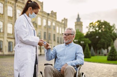 Koruyucu yüz maskesi takan kadın doktor nabız ve oksijen seviyelerini parmak ucu nabız oksimetresi kullanarak ölçüyor.