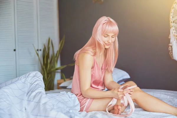 Jonge vrouw met lang roze haar in zijden pyjama leest bericht op groot bed — Stockfoto