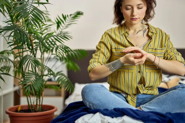 Jonge vrouw in casual dragen zittend op bed, ontspannen in yoga Lotus pose, doen sommige meditatie thuis — Stockfoto