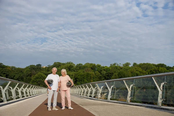 Paspaslı ve kulaklıklı yaşlı çift yaya köprüsünde duruyor. — Stok fotoğraf