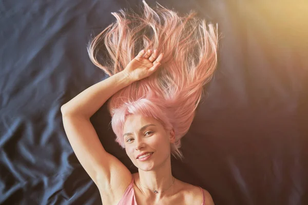Mooie vrouw met lang los roze haar en zilveren sieraden ligt op zacht comfortabel bed — Stockfoto