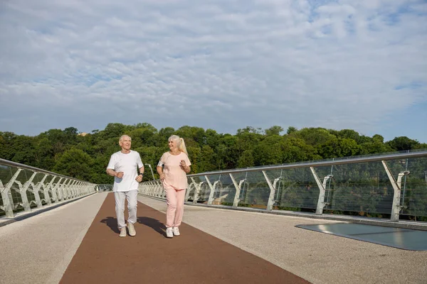 Sonriendo hombre y mujer mayores con teléfono móvil a lo largo de pasarela — Foto de Stock