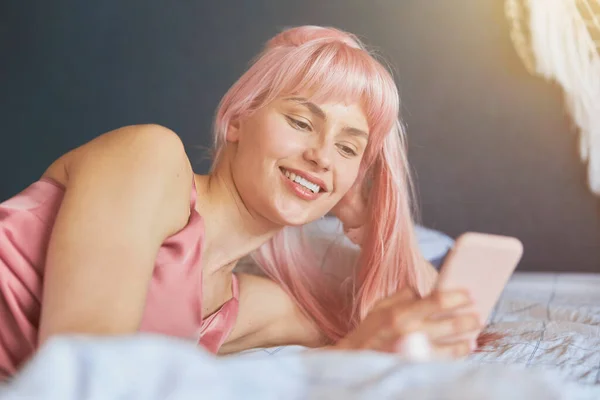 Junge Frau mit hellen Haaren blickt auf Handy-Bildschirm im Bett — Stockfoto