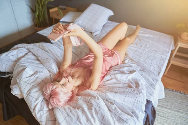 Mooie gelukkig dame in elegante zijde kleding neemt selfie liggend op groot bed — Stockfoto
