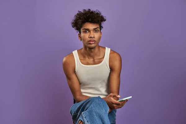 Retrato de primer plano del joven sentado con cámara móvil y mirando sobre fondo púrpura aislado —  Fotos de Stock
