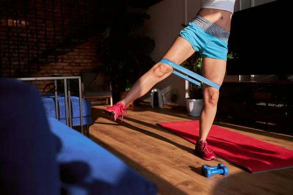 Sportliche Frau in blauen Shorts macht Seitenbeinheben mit Gummiband zu Hause — Stockfoto