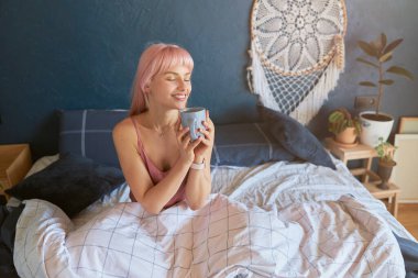 Güzel bayan, tembel bir sabahta rahat bir yatakta otururken fincanı tutuyor.