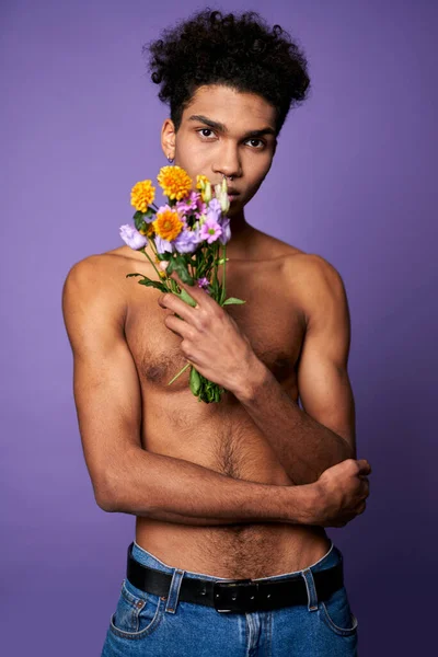 Bonito modelo transexual jovem com flores na mão em pé sobre fundo roxo. Moda glamour — Fotografia de Stock