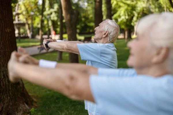 Grauhaariger älterer Mann trainiert mit Frau auf Wiese im Stadtpark — Stockfoto