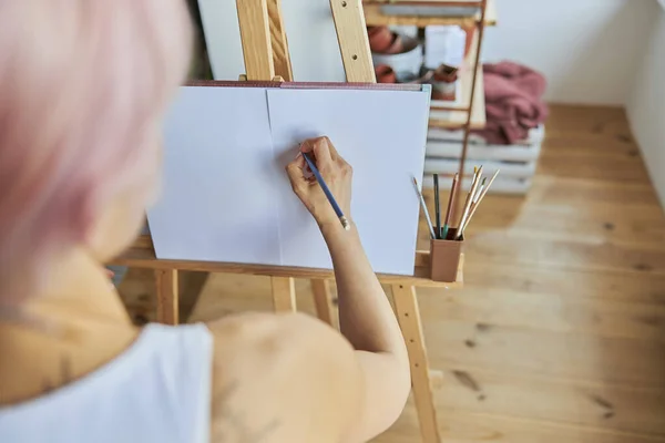 Pelukis wanita menggunakan pensil grafit untuk menggambar pada kertas kosong di kayu easel — Stok Foto