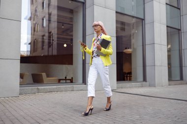 Bir kadın akıllı telefonuyla sokakta yürürken bir şeyler taşıyor.