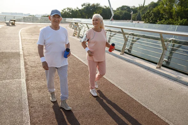 Gülümseyen yaşlı bayan ve şişeli adam şehir köprüsünde birlikte yürüyorlar. — Stok fotoğraf