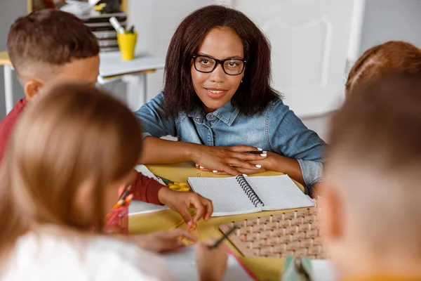 Smiling teacher looking at schoolchildren during lesson — Stock Photo, Image