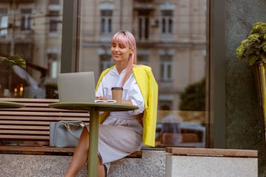 Dışarıdaki kafede dizüstü bilgisayarda çalışan neşeli kadın.
