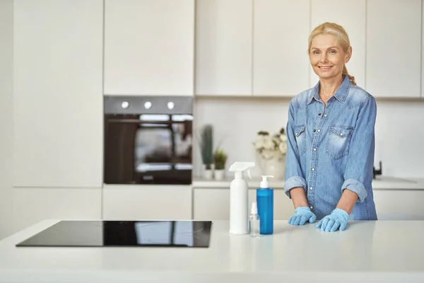 Lastik eldivenli gülümseyen kadın mutfakta temizlenmeye hazır. Deterjan, dezenfektan spreyi ve şişenin içine jöle. — Stok fotoğraf