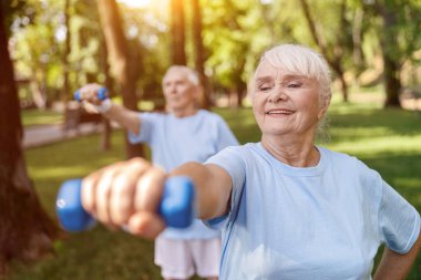 Güçlü kıdemli kadın, Yeşil Park 'ta kocasıyla dambıl eğitimi yapıyor.