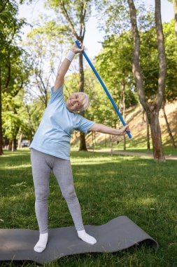 Eşofmanlı yaşlı bayan yeşil parkta duran plastik barla yan eğilmiş.