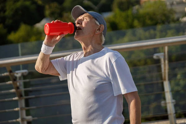 Senior gentleman dricker vatten från flaskan står på bryggan vid träning — Stockfoto