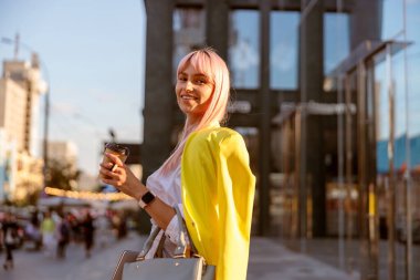 Neşeli bir kadın sokakta durup elinde bir fincan kahve tutuyor.