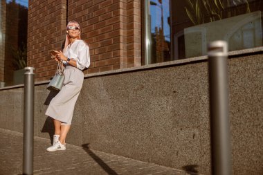 Sokakta cep telefonu kullanan neşeli genç bir kadın.