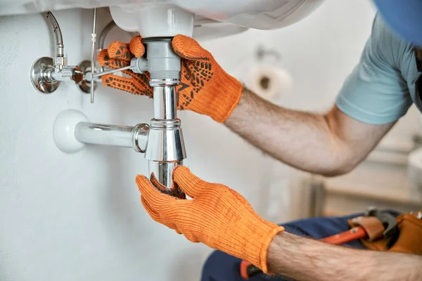 Erkek tesisatçı elleri metal lavabo borusunu tamir ediyor.