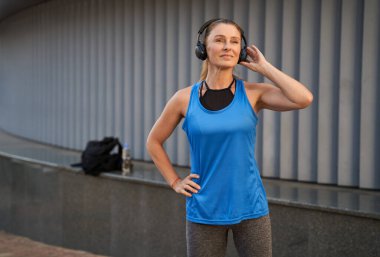 Spor giyim ve kulaklıklarda rahat orta yaşlı sporcu kadın dışarıda egzersiz yaparken müzik veya podcast dinliyor.