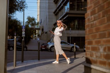 Neşeli bir kadın sokakta durup müzik dinliyor.