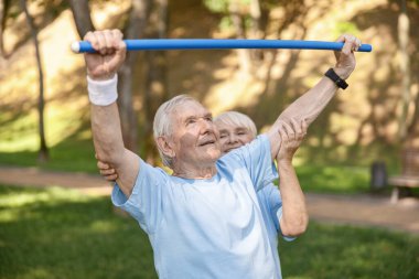 Kıdemli kadın çalıştırıcı yeşil parktaki barda erkeğin egzersiz yapmasına yardım ediyor.