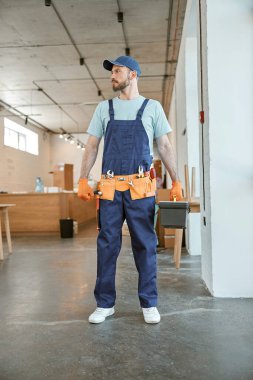 Sakallı erkek işçi, elinde aletlerle plastik kutu tutuyor.