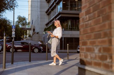 Neşeli bir kadın sokakta yürüyor ve müzik dinliyor.