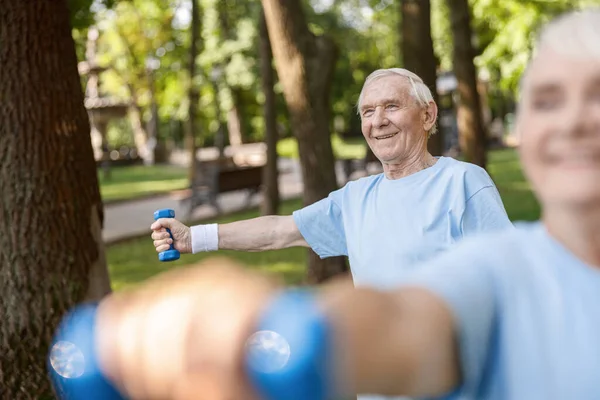 Χαρούμενος ώριμος άντρας κάνει αθλητικές ασκήσεις με dumbbell κατάρτισης με γυναίκα στο πάρκο — Φωτογραφία Αρχείου