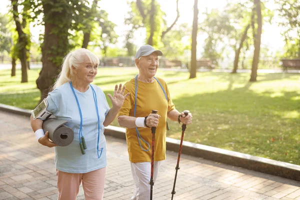 Positive Seniorin mit Matte und Mann mit Stöcken für Nordic Walking im grünen Park — Stockfoto
