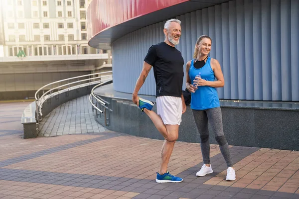 Full length shot of joyful middle aged couple, man and woman in sportswear smiling away, standing together outdoors ready for workout