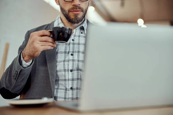 Pria berjenggot minum kopi dan menggunakan laptop di kafe — Stok Foto