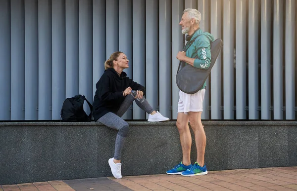 Orta yaşlı sporcular, spor kıyafetli kadın ve erkek dışarıda spor yapmayı beklerken sohbet ediyorlar.