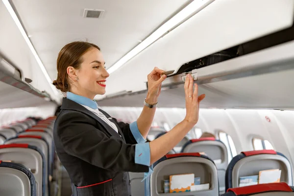 Alegre auxiliar de vuelo cerrando la papelera de equipaje en el avión — Foto de Stock