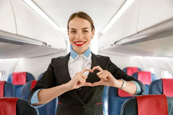 Veselá letuška dělá srdeční znamení v letadle — Stock fotografie