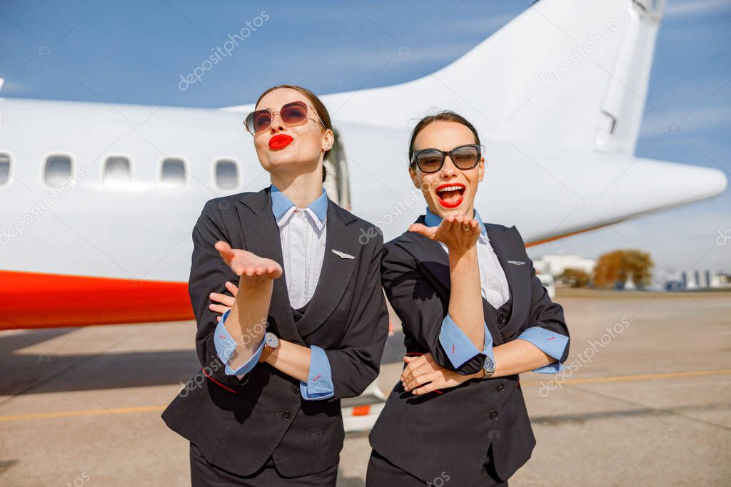 Cheerful women stewardesses sending blow kiss at airport