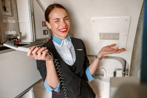 Assistente de bordo alegre com telefone em pé na cabine da aeronave — Fotografia de Stock