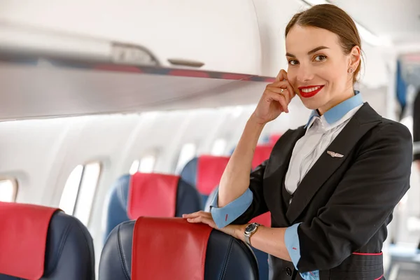 Alegre azafata de pie junto a la papelera de equipaje en los aviones — Foto de Stock